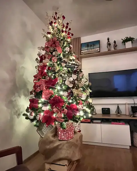 Árvore acesa com poinsétias vermelhas e frutinhas douradas ao lado da TV