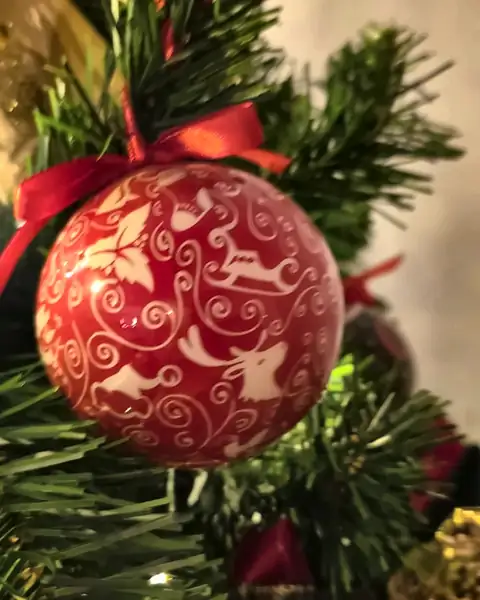Bola vermelha com arabescos brancos e laço vermelho na árvore