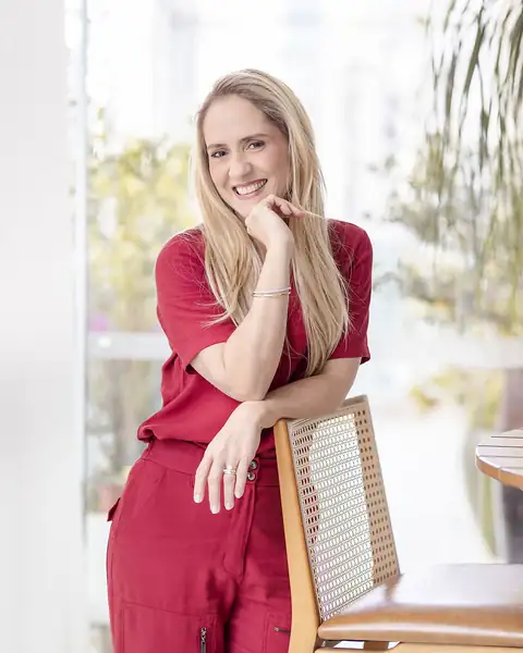 Margot, de macacão vermelho, sorrindo apoiada numa cadeira